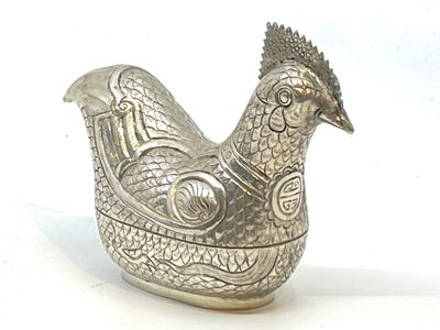 une figurine de poulet en argent posée sur une surface blanche