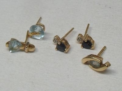 trois paires de boucles d'oreilles à clous en or et pierres bleues sur un fond blanc