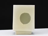 a small white vase with a green spot on it