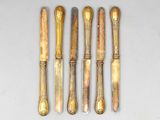 six silverware spoons and a knife are lined up on a white surface