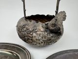 a silver bowl with a bird on it next to a silver plate