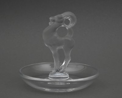une figurine en verre représentant un bélier, posée sur une assiette en verre