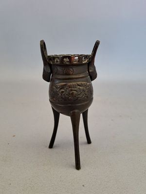 un petit vase en bronze posé sur un socle, sur une surface blanche