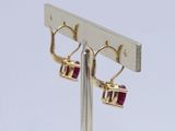 pair of gold and ruby earrings on a silver stand