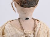 an old fashioned doll with a chain around her neck and a necklace around her neck