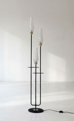 deux grands lampadaires en verre posés sur un pied noir dans une pièce blanche