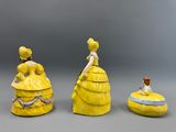 trois figurines représentant des femmes en robe jaune sont assises les unes à côté des autres