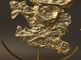 gold sculpture of a dragon with horns on a stand on a gray background
