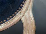 the back of a blue velvet chair with a wooden frame and beaded trim