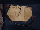 tan leather handbag with brown leather strap on a blue carpet