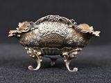 a silver bowl on a stand on a black surface