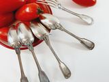 a bowl of spoons and forks with tomatoes on the table