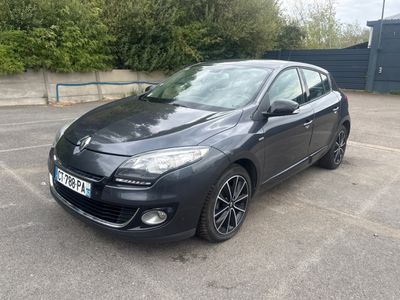 La voiture noire est garée sur le parking, à côté d'une clôture.