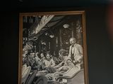 a black and white photo of a man sitting at a table in front of a picture