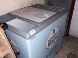 a blue refrigerator sitting in the corner of a room next to a pile of wood