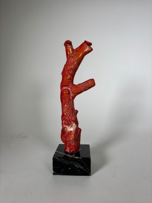 une image représentant une sculpture rouge représentant une branche d'arbre posée sur un socle en marbre