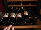 many bottles of wine in a wine cooler with a hand reaching for one