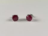 une paire de boucles d'oreilles à clous ornées de rubis, posées sur un fond blanc