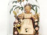 une figurine représentant une petite fille assise sur une chaise sous une cloche en verre