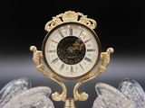 a gold clock on a stand with wings on it