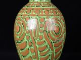 un vase vert et orange posé sur une surface noire