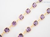 a close up of a necklace with purple stones on a white surface