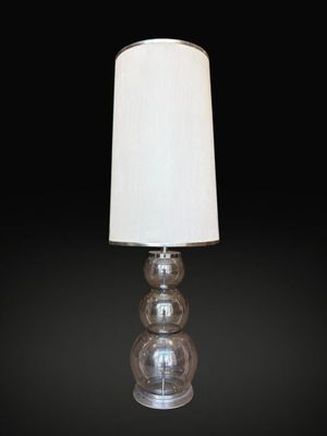 a clear glass lamp with a white shade on a black background