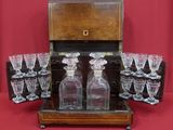 des bouteilles et des verres dans un coffret en bois posé sur un fond rouge