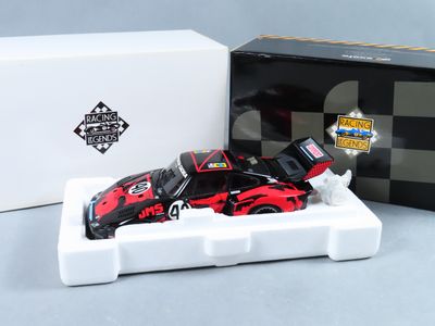 une petite voiture rouge et noire dans une boîte blanche, à côté d'une boîte noire et blanche