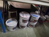 several buckets of paint sitting on the floor under a shelf