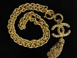 a gold chain necklace with a tassel charm on a black background