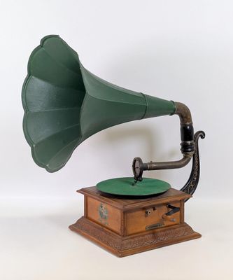 un vieux gramophone vert posé sur un support en bois, devant un fond blanc