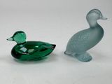 two glass ducks sitting next to each other on a white surface