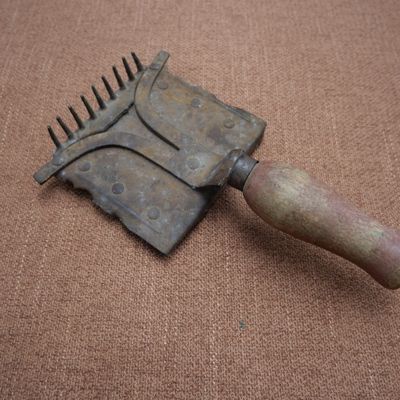 une petite brosse métallique avec un manche en bois posée sur une surface marron