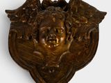 une image représentant une plaque en bronze sur laquelle figurent un visage et des ailes