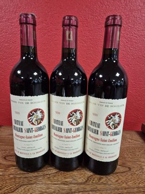 trois bouteilles de vin sont posées sur une table devant un mur rouge
