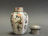 a white vase with a bird on it next to a silver container