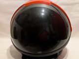un casque noir et orange posé sur un support, sur fond blanc