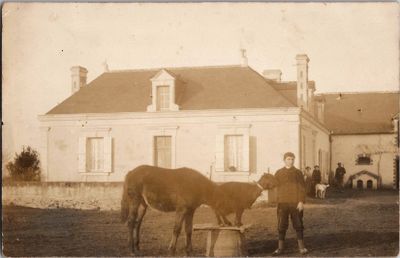 une vieille photo représentant un homme et un cheval devant une maison