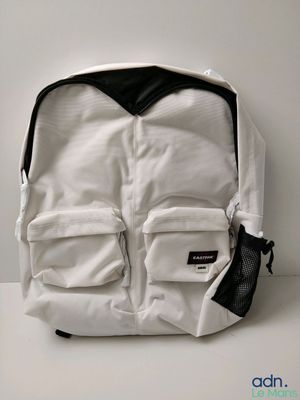 un sac à dos blanc posé sur une surface blanche, avec un sac en filet noir à côté