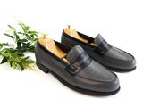 black leather loafer shoes with a plant on a white background