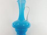 a blue glass vase with a white handle on a white background