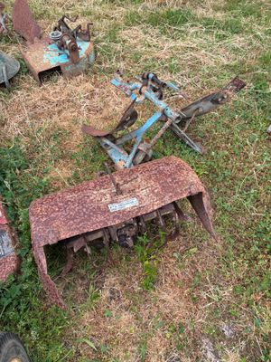Plusieurs vieux outils agricoles sont posés dans l'herbe, à même le sol.