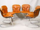 quatre fauteuils en cuir orange et une table aux pieds chromés