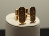 two gold cufflinks with egyptian symbols on them on a white stand