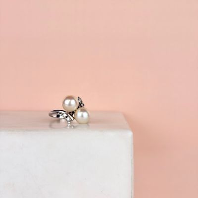 un gros plan d'une bague en perle et argent posée sur un bloc de marbre