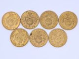 six gold sovereigns of different sizes and shapes on a white surface