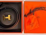 une boîte orange ornée d'une ceinture noire et d'un logo « h » doré