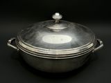 une cocotte ancienne en métal argenté avec un couvercle, sur fond noir