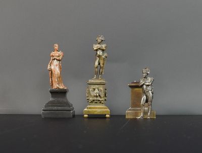 trois statues d'hommes et de femmes posées sur des socles, sur un fond noir